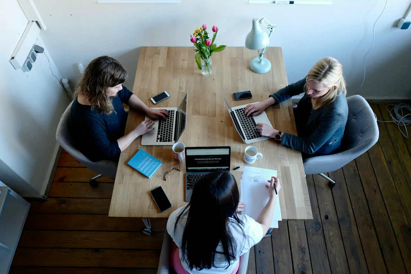Three people working on laptops around a wooden table, seen from above