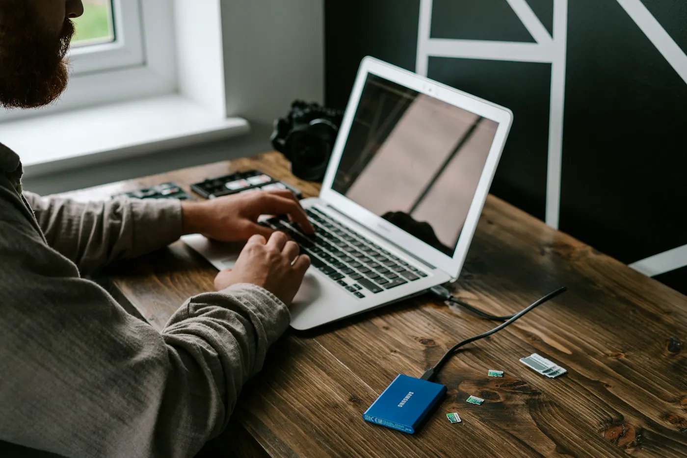 A person typing on a laptop with a small portable drive connected beside it