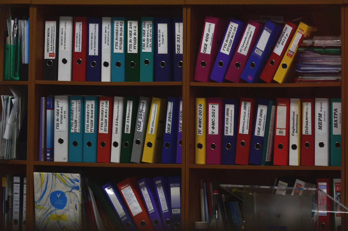 Rows of coloured ring binders on wooden office shelves