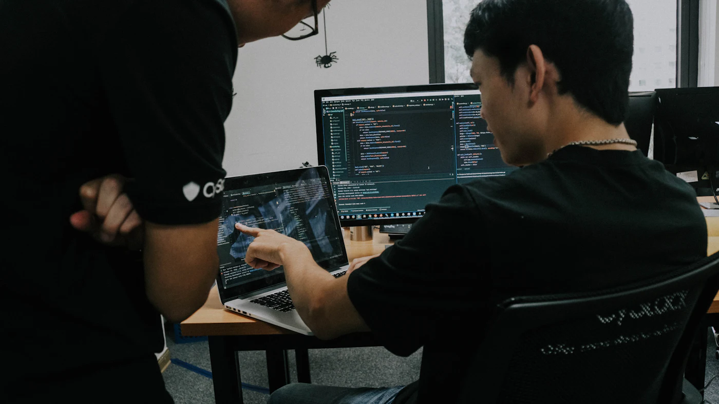 Two men working side by side at computers in an office