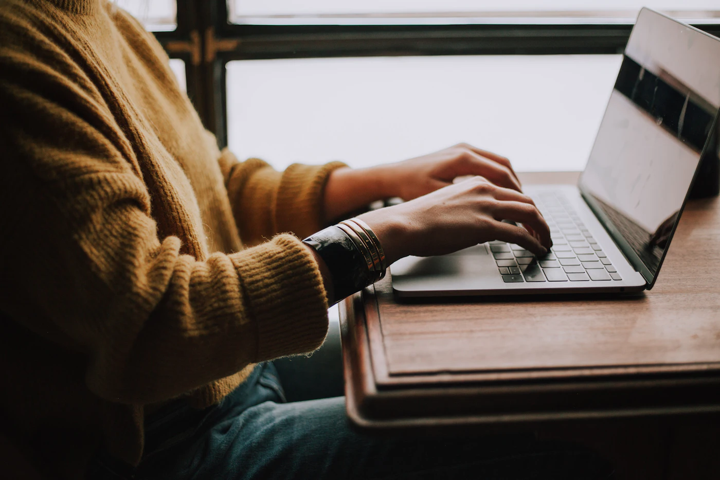 A person typing on a laptop on a bed