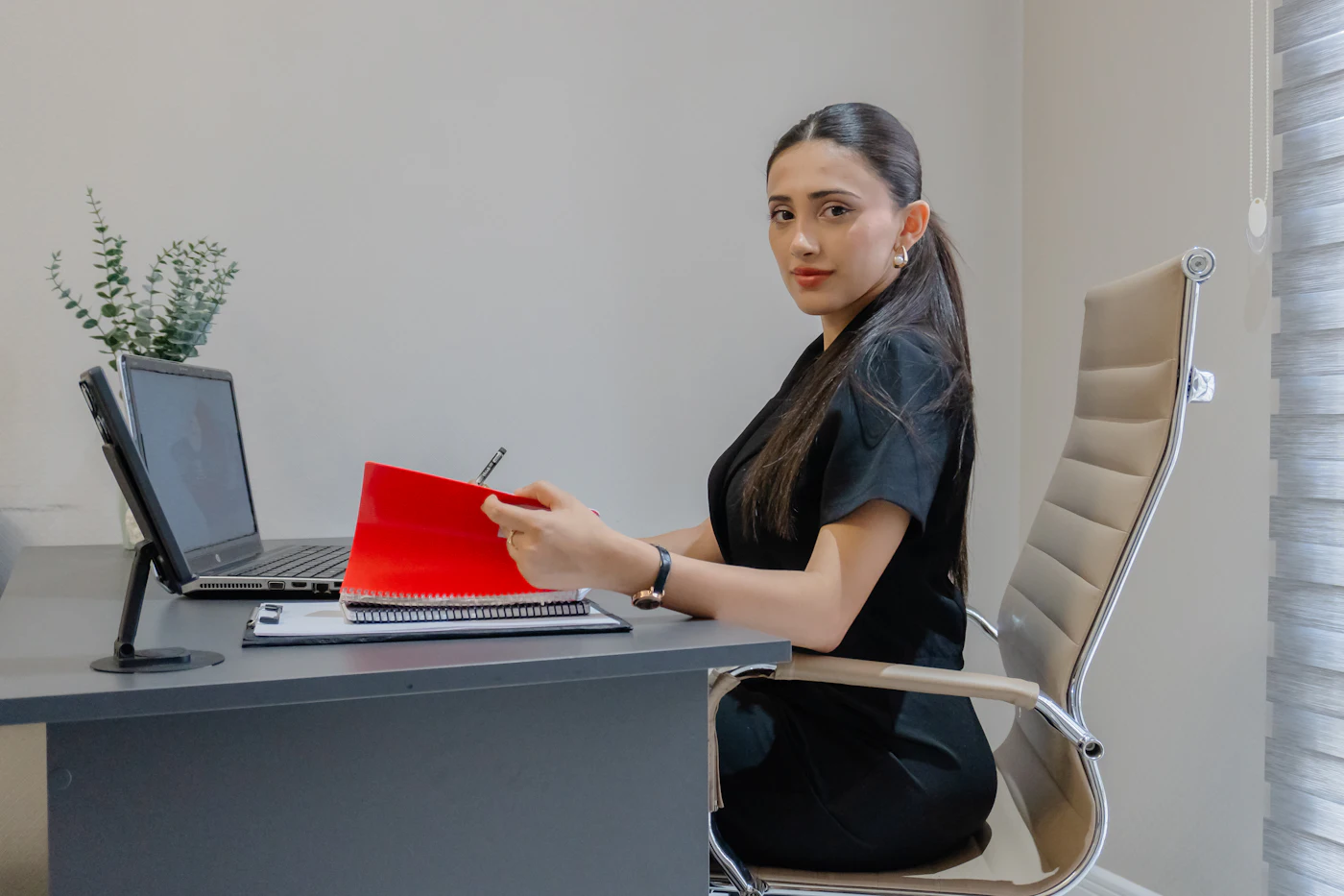 A woman working at a desk with a laptop and a red folder