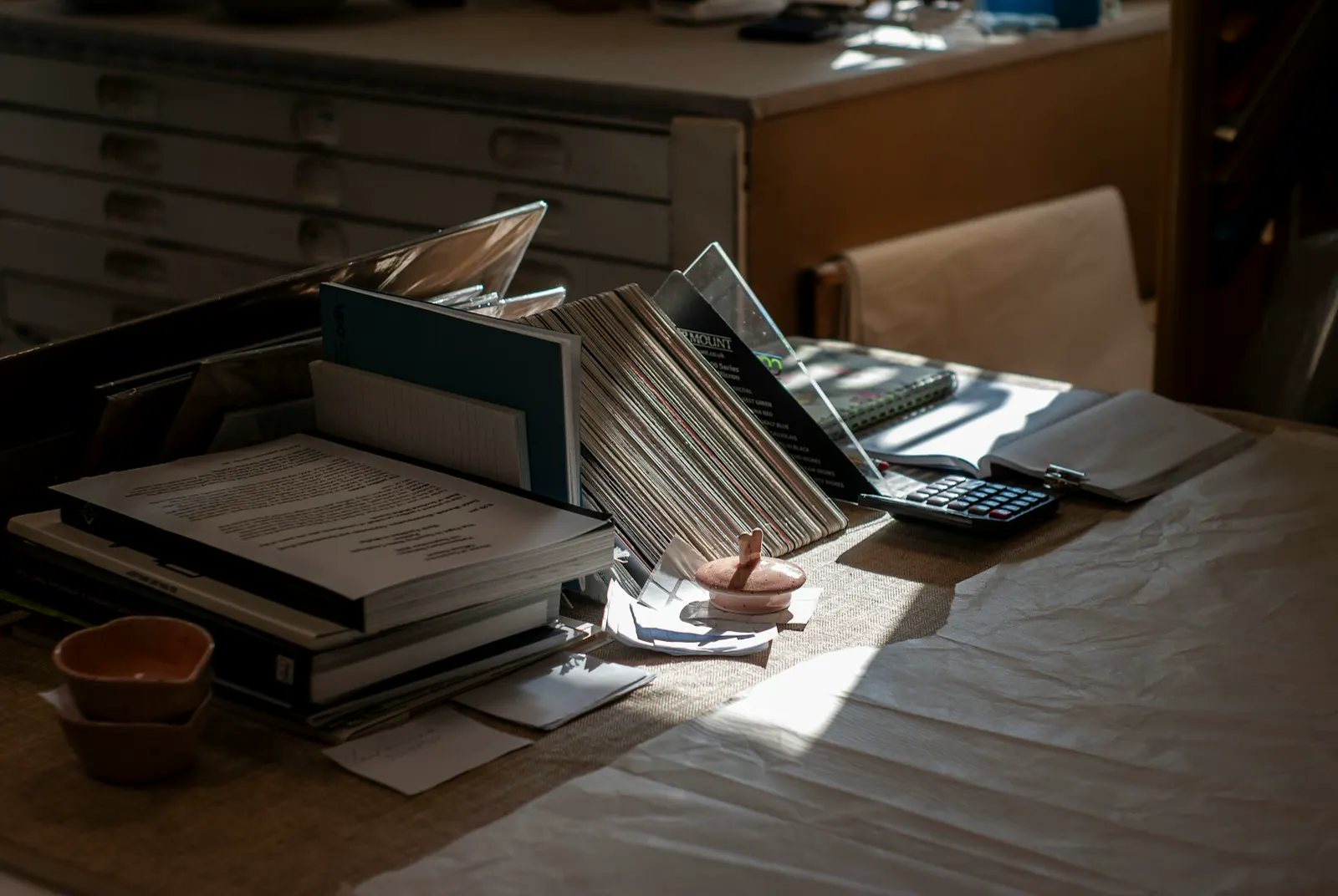 A cluttered desk with stacked files, papers and a calculator